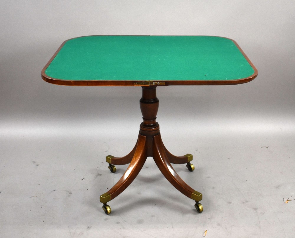 A Regency mahogany card table featuring a folding swivel top, a turned central pedestal column, and four splayed sabre legs with brass castors. View IV