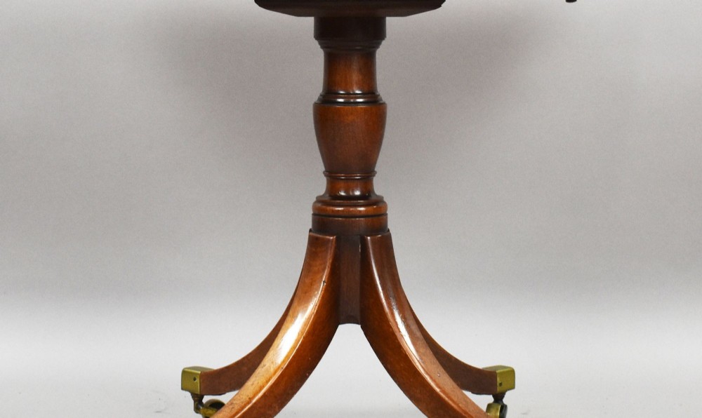 A Regency mahogany card table featuring a folding swivel top, a turned central pedestal column, and four splayed sabre legs with brass castors. View IX