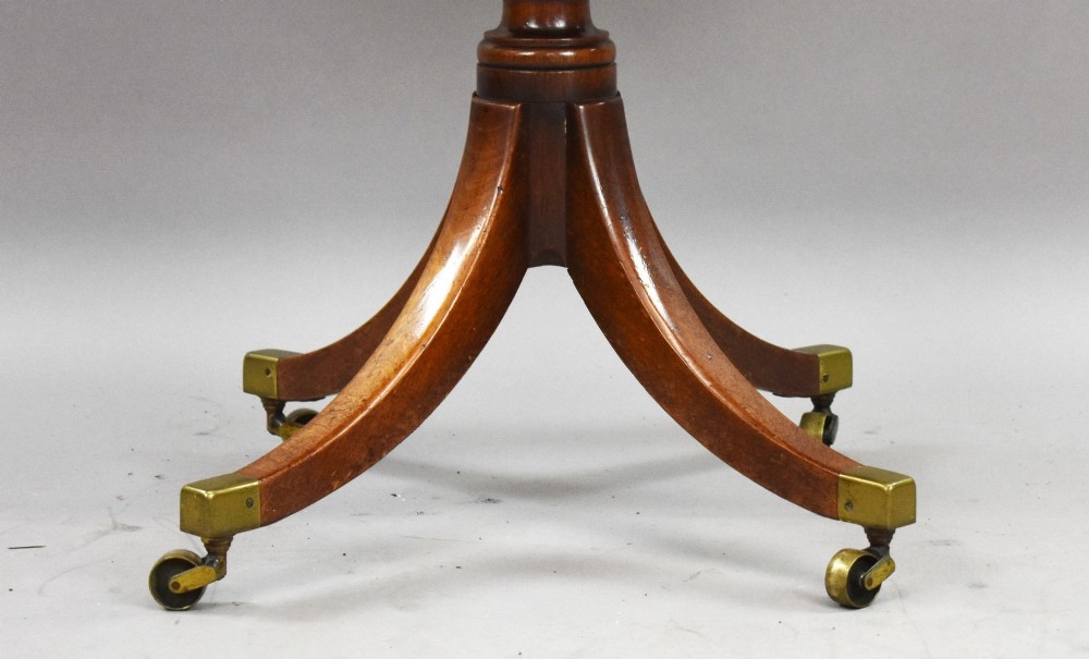 A Regency mahogany card table featuring a folding swivel top, a turned central pedestal column, and four splayed sabre legs with brass castors. View X