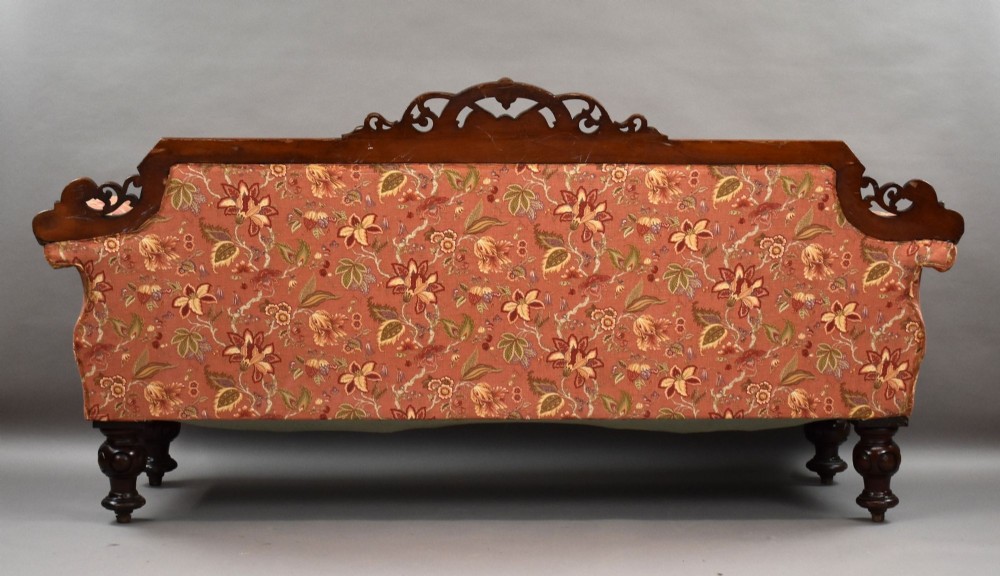 Victorian mahogany settee featuring carved scroll cresting along the top rail, button-tufted floral fabric upholstery, rolled armrests, and turned wooden front legs. View IV