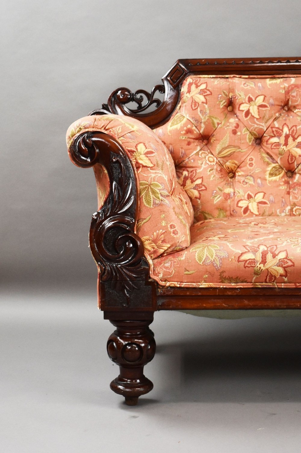 Victorian mahogany settee featuring carved scroll cresting along the top rail, button-tufted floral fabric upholstery, rolled armrests, and turned wooden front legs. View V