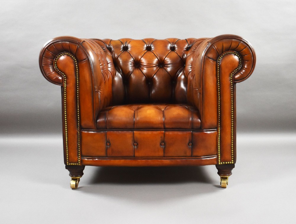 A matching pair of warm brown leather Chesterfield armchairs featuring deep button tufting, brass studding, rolled arms, and brass castors. View VII