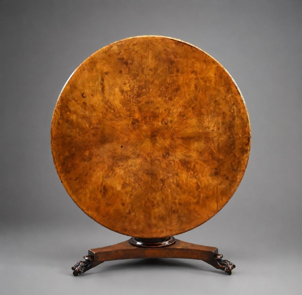 A circular Regency breakfast table with a figured burr elm veneered top displayed upright on a wooden pedestal base.