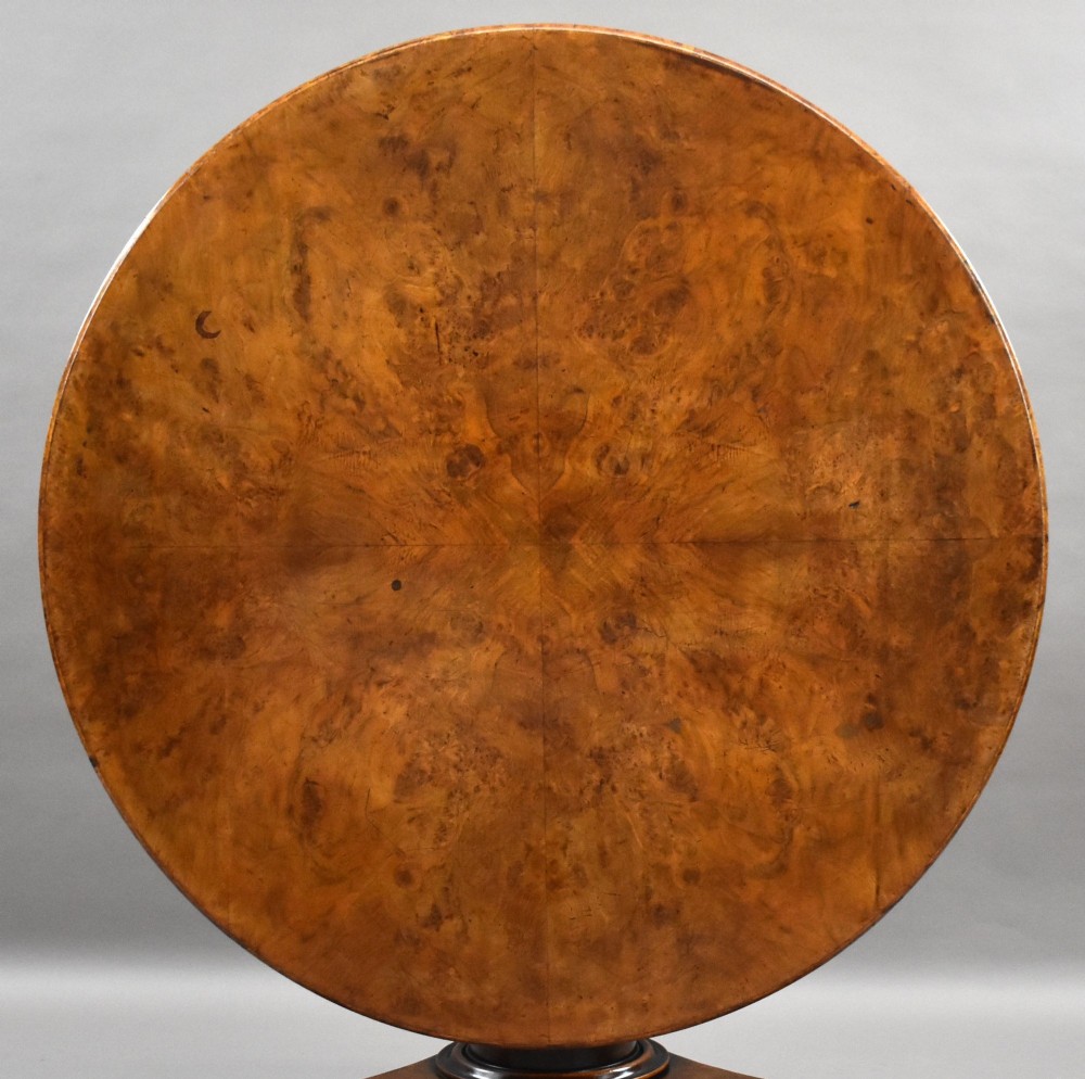 A circular Regency breakfast table with a figured burr elm veneered top displayed upright on a wooden pedestal base. View II