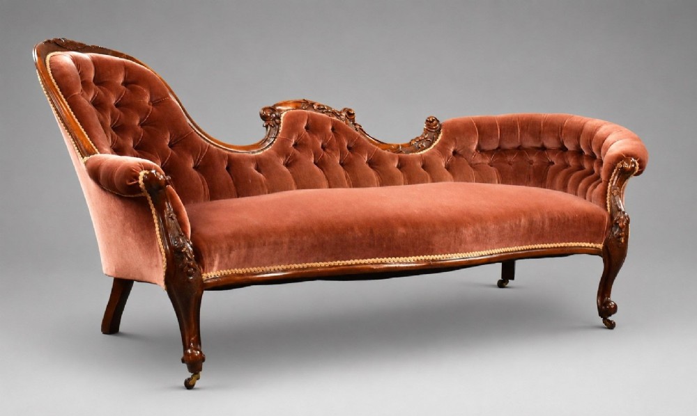 A Victorian carved walnut chaise longue upholstered in deep-buttoned rose pink velvet with cabriole legs on brass castors.