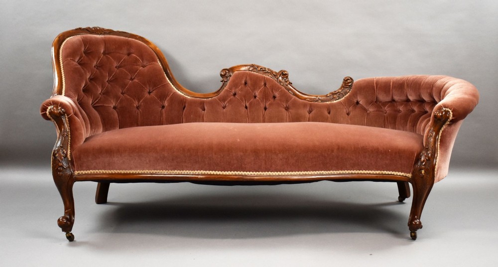 A Victorian carved walnut chaise longue upholstered in deep-buttoned rose pink velvet with cabriole legs on brass castors. View II