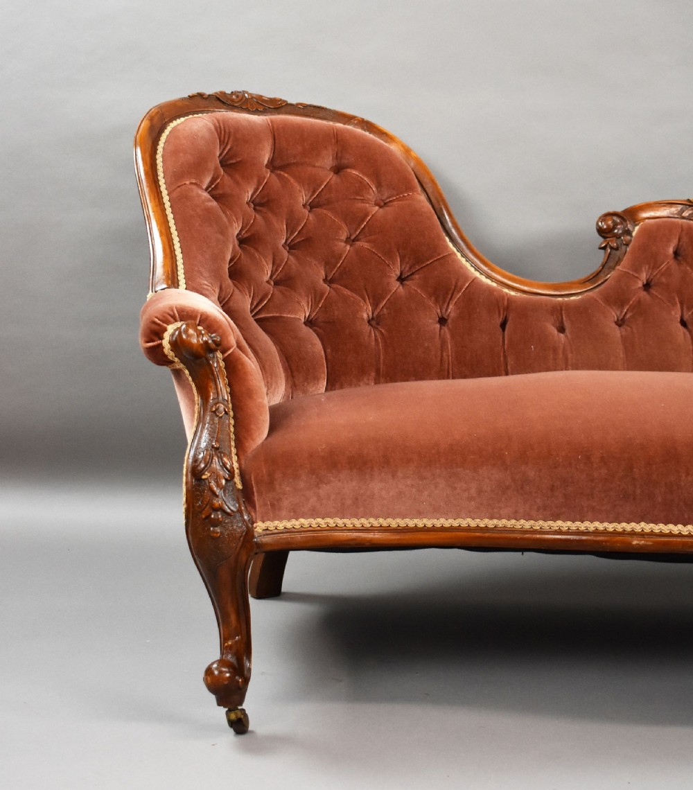 A Victorian carved walnut chaise longue upholstered in deep-buttoned rose pink velvet with cabriole legs on brass castors. View III