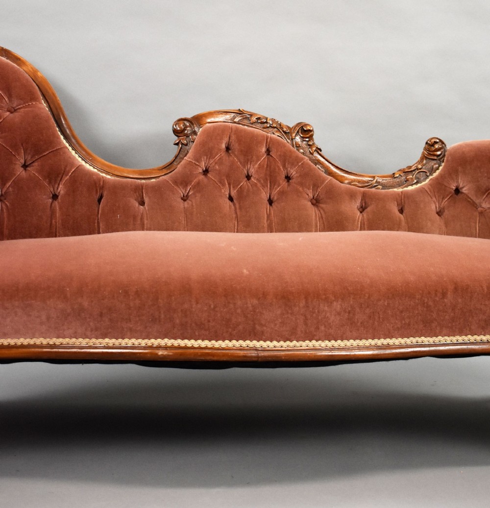 A Victorian carved walnut chaise longue upholstered in deep-buttoned rose pink velvet with cabriole legs on brass castors. View IV