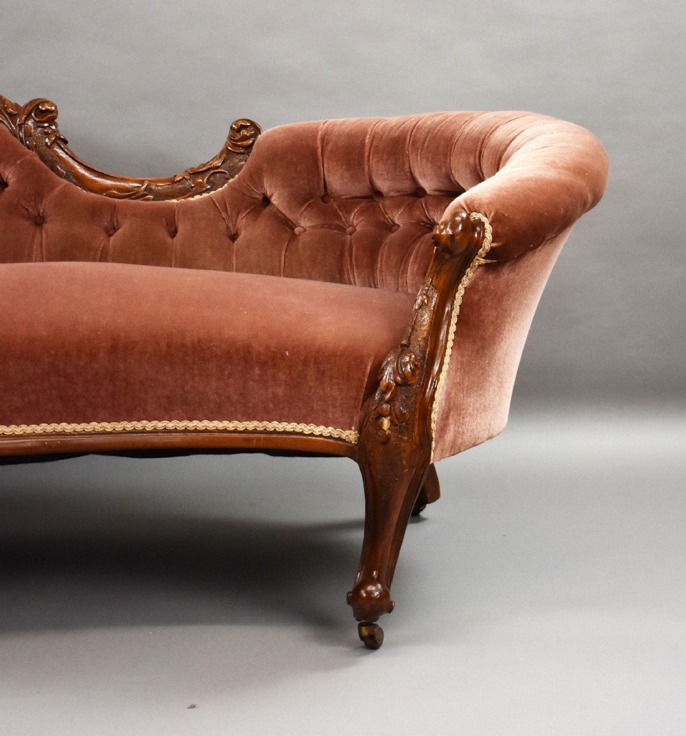 A Victorian carved walnut chaise longue upholstered in deep-buttoned rose pink velvet with cabriole legs on brass castors. View V
