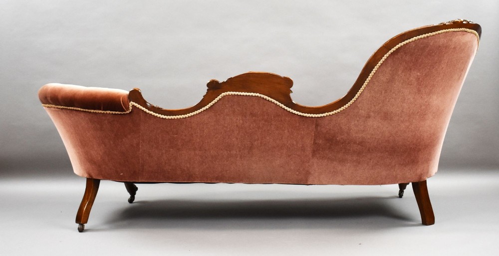 A Victorian carved walnut chaise longue upholstered in deep-buttoned rose pink velvet with cabriole legs on brass castors. View VII