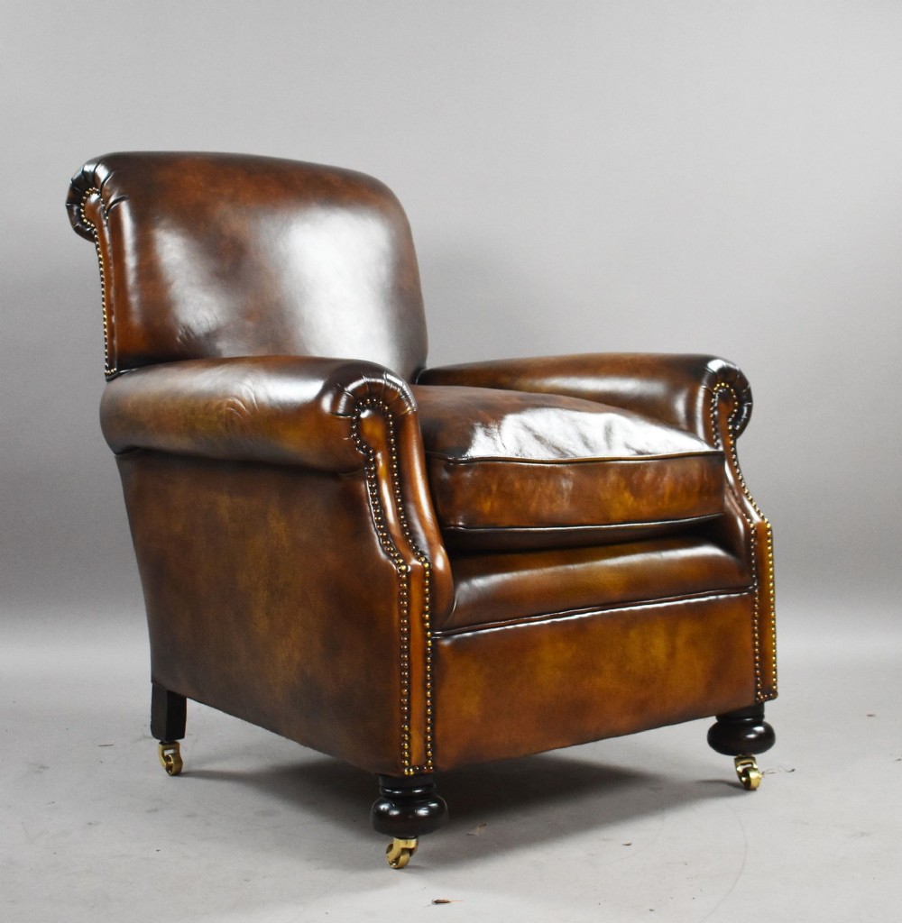 A pair of antique chestnut brown leather club chairs featuring rolled arms, brass stud trimming, loose cushion seats, and dark turned legs on brass castors. View VI