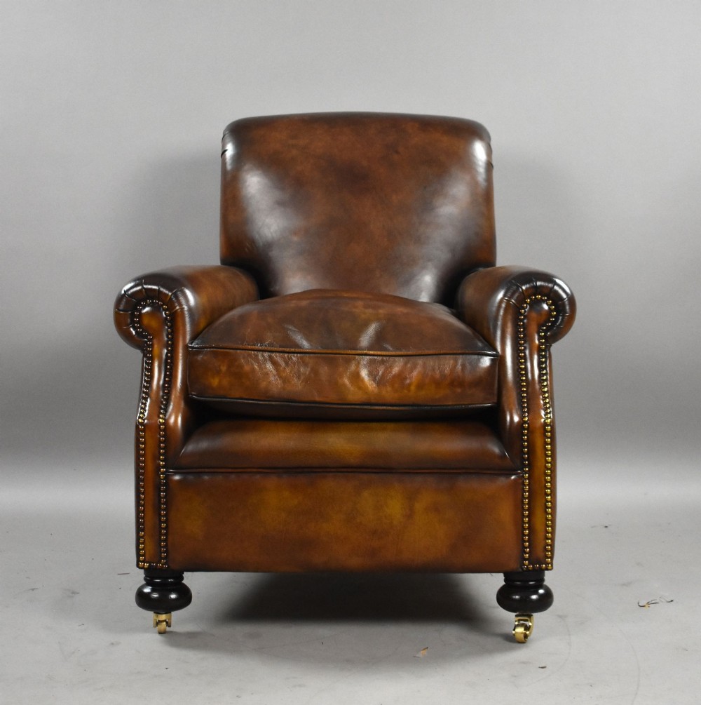 A pair of antique chestnut brown leather club chairs featuring rolled arms, brass stud trimming, loose cushion seats, and dark turned legs on brass castors. View VII