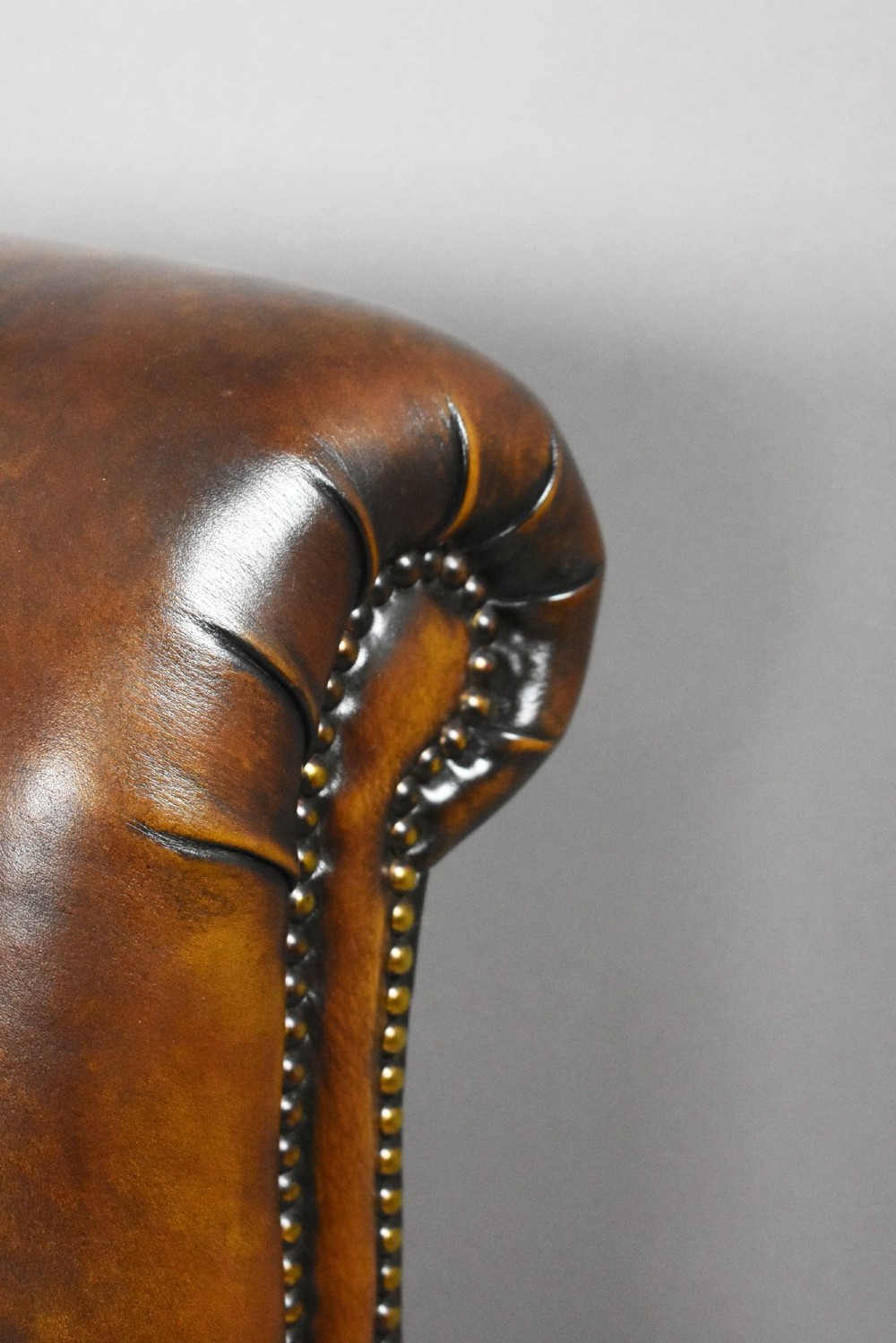 A pair of antique chestnut brown leather club chairs featuring rolled arms, brass stud trimming, loose cushion seats, and dark turned legs on brass castors. View IX