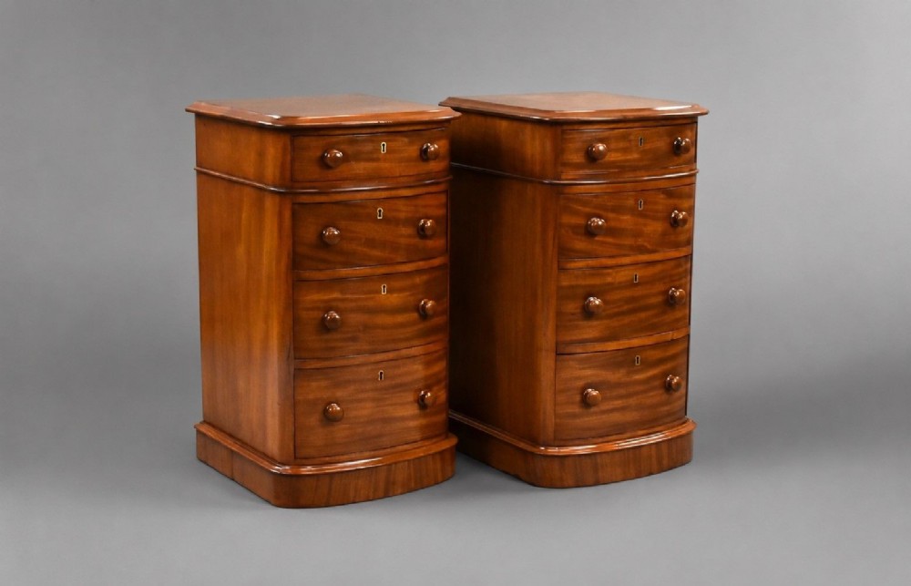 A matching pair of four-drawer Victorian mahogany bedside chests featuring curved fronted drawers, turned wooden handles, and plinth bases.