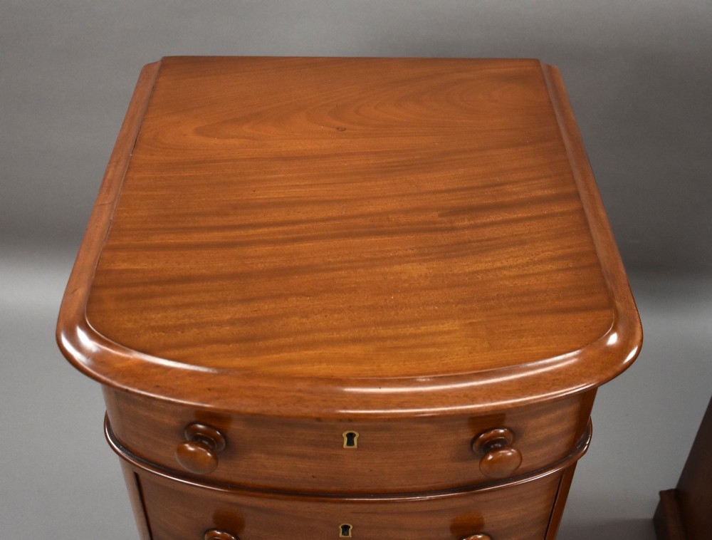 A matching pair of four-drawer Victorian mahogany bedside chests featuring curved fronted drawers, turned wooden handles, and plinth bases. View V