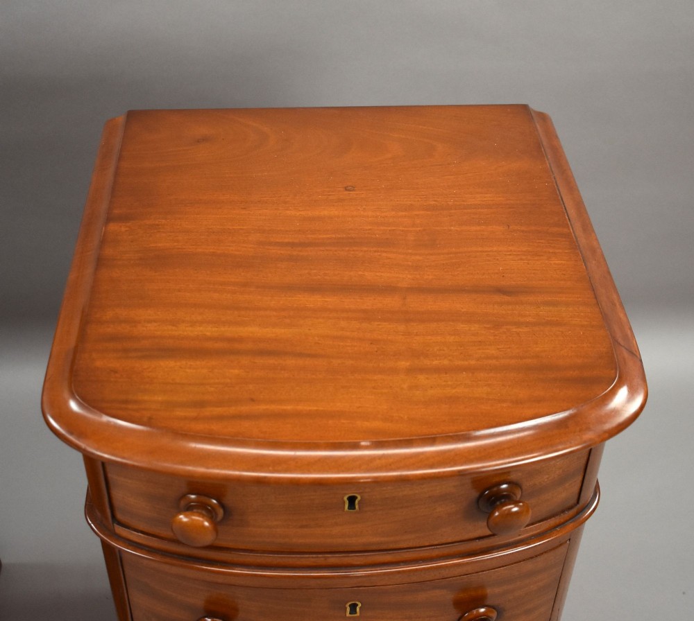 A matching pair of four-drawer Victorian mahogany bedside chests featuring curved fronted drawers, turned wooden handles, and plinth bases. View VI