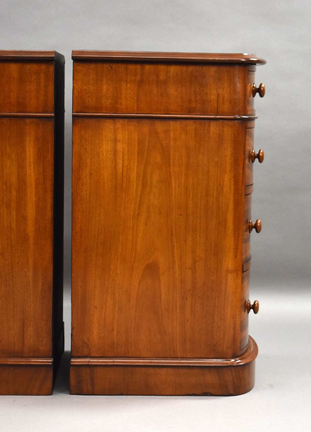 A matching pair of four-drawer Victorian mahogany bedside chests featuring curved fronted drawers, turned wooden handles, and plinth bases. View X