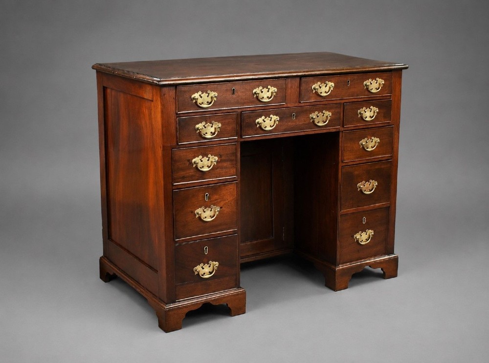 A George III mahogany kneehole desk featuring a flat rectangular top, brass swan-neck handles on multiple drawers, a central recessed cupboard, and bracket feet.