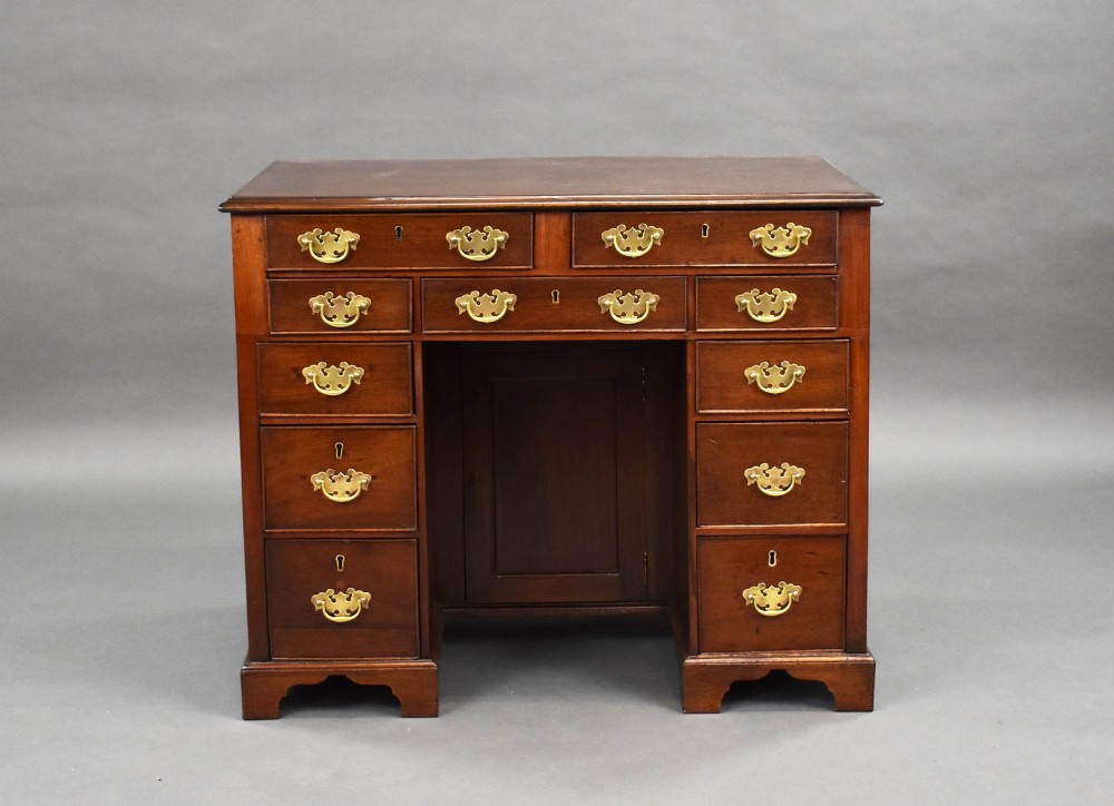 A George III mahogany kneehole desk featuring a flat rectangular top, brass swan-neck handles on multiple drawers, a central recessed cupboard, and bracket feet. View II