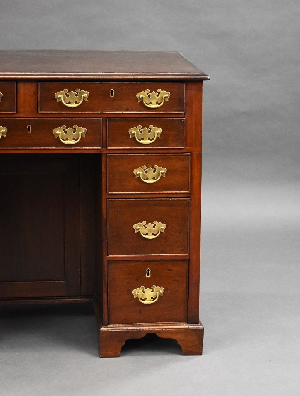 A George III mahogany kneehole desk featuring a flat rectangular top, brass swan-neck handles on multiple drawers, a central recessed cupboard, and bracket feet. View IV