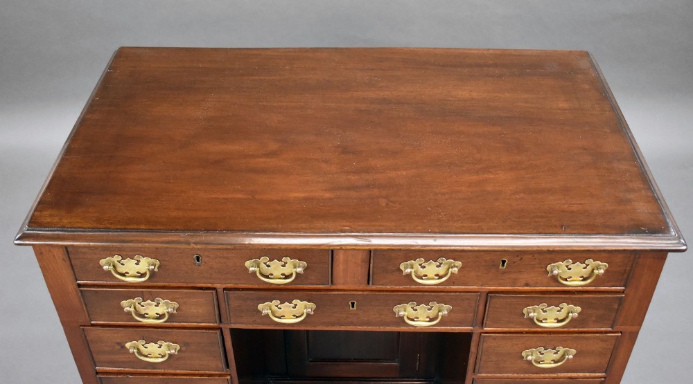 A George III mahogany kneehole desk featuring a flat rectangular top, brass swan-neck handles on multiple drawers, a central recessed cupboard, and bracket feet. View V