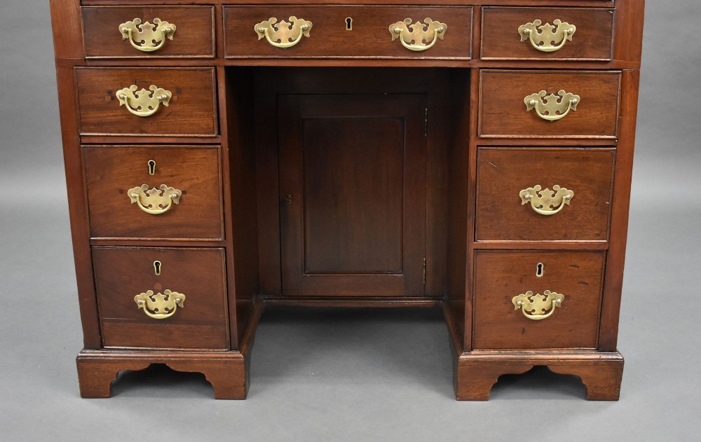 A George III mahogany kneehole desk featuring a flat rectangular top, brass swan-neck handles on multiple drawers, a central recessed cupboard, and bracket feet. View VI