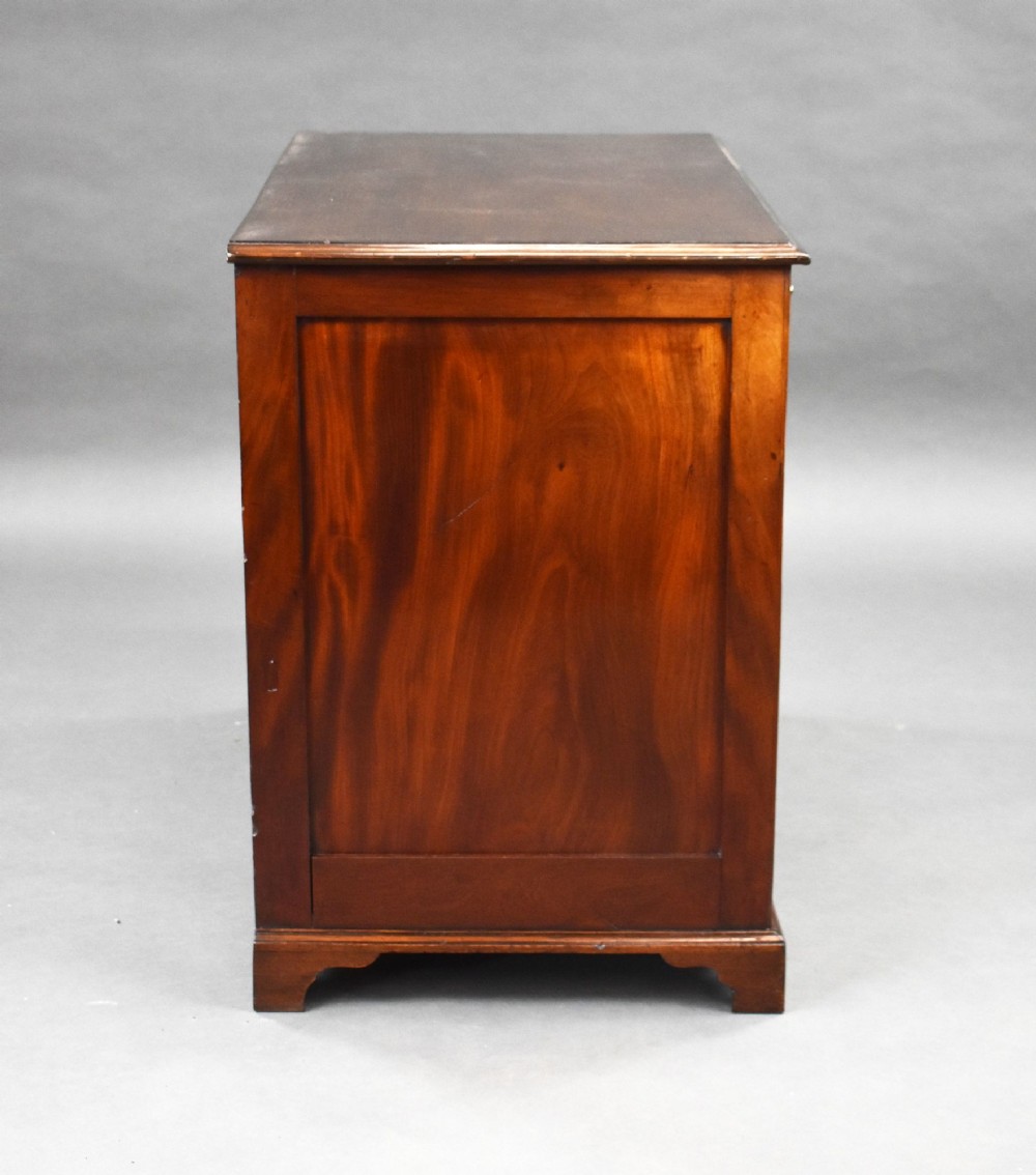 A George III mahogany kneehole desk featuring a flat rectangular top, brass swan-neck handles on multiple drawers, a central recessed cupboard, and bracket feet. View VII