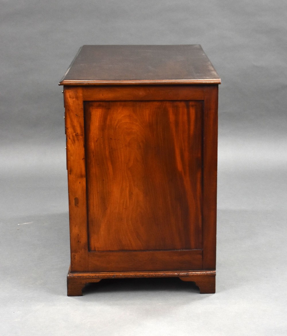 A George III mahogany kneehole desk featuring a flat rectangular top, brass swan-neck handles on multiple drawers, a central recessed cupboard, and bracket feet. View VIII