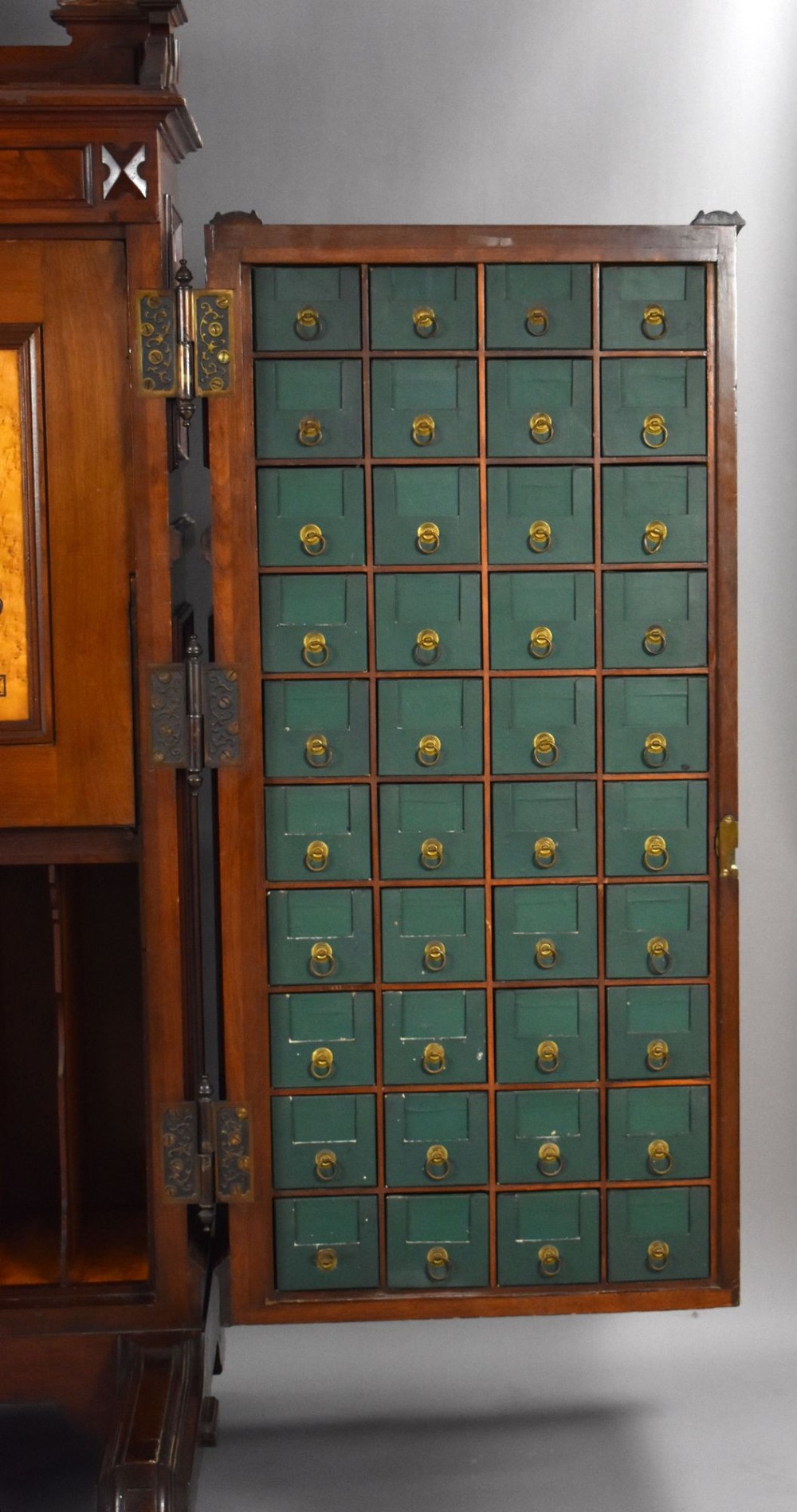 A Victorian walnut Wooton secretary desk featuring carved cresting, curved upper doors, panelling, brass mail slots, and carved feet on castors. View V