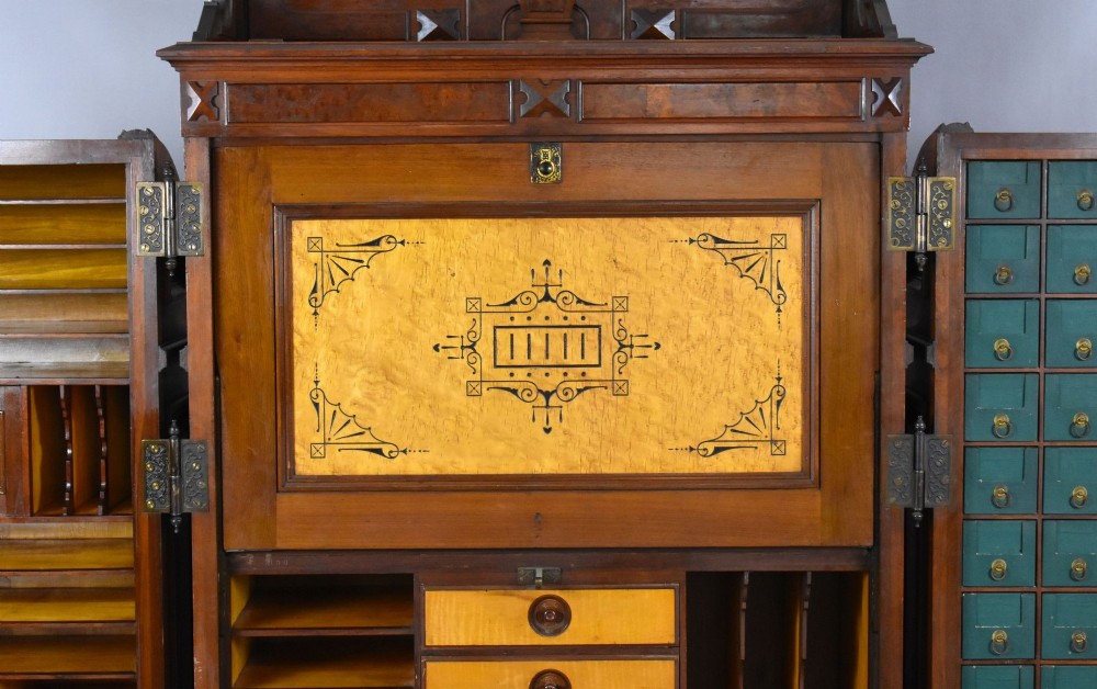 A Victorian walnut Wooton secretary desk featuring carved cresting, curved upper doors, panelling, brass mail slots, and carved feet on castors. View VII
