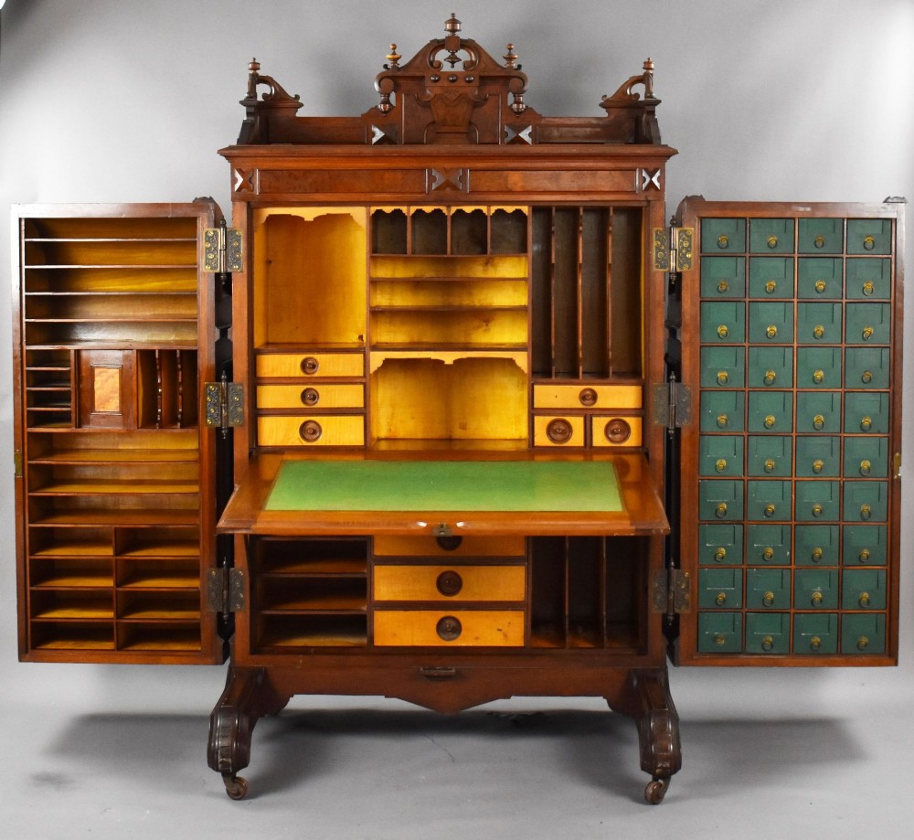 A Victorian walnut Wooton secretary desk featuring carved cresting, curved upper doors, panelling, brass mail slots, and carved feet on castors. View IX