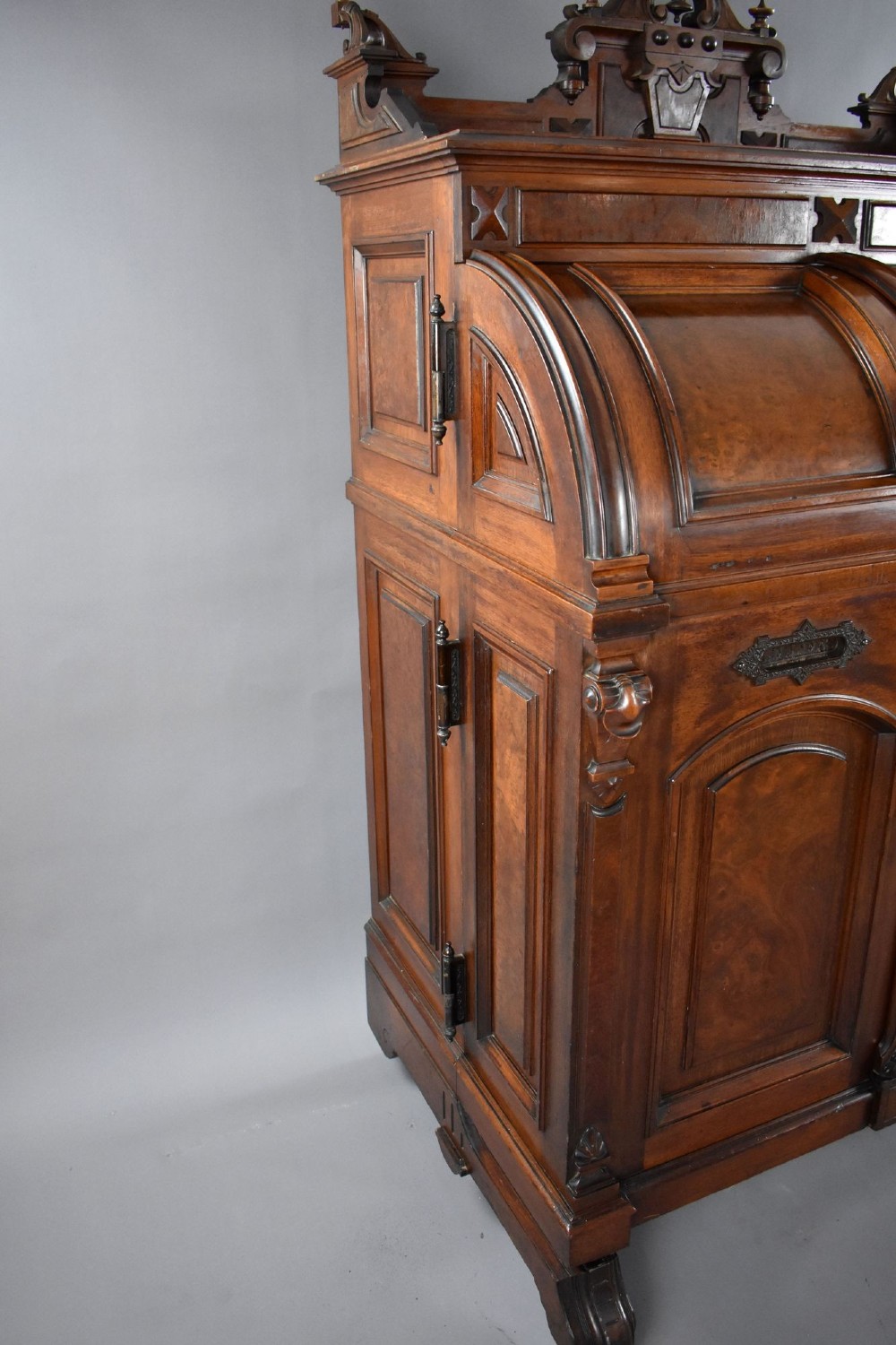 A Victorian walnut Wooton secretary desk featuring carved cresting, curved upper doors, panelling, brass mail slots, and carved feet on castors. View XIII