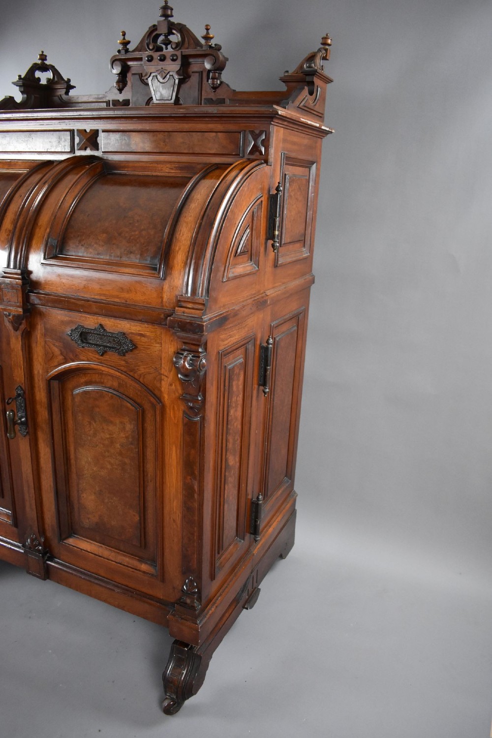 A Victorian walnut Wooton secretary desk featuring carved cresting, curved upper doors, panelling, brass mail slots, and carved feet on castors. View XIV