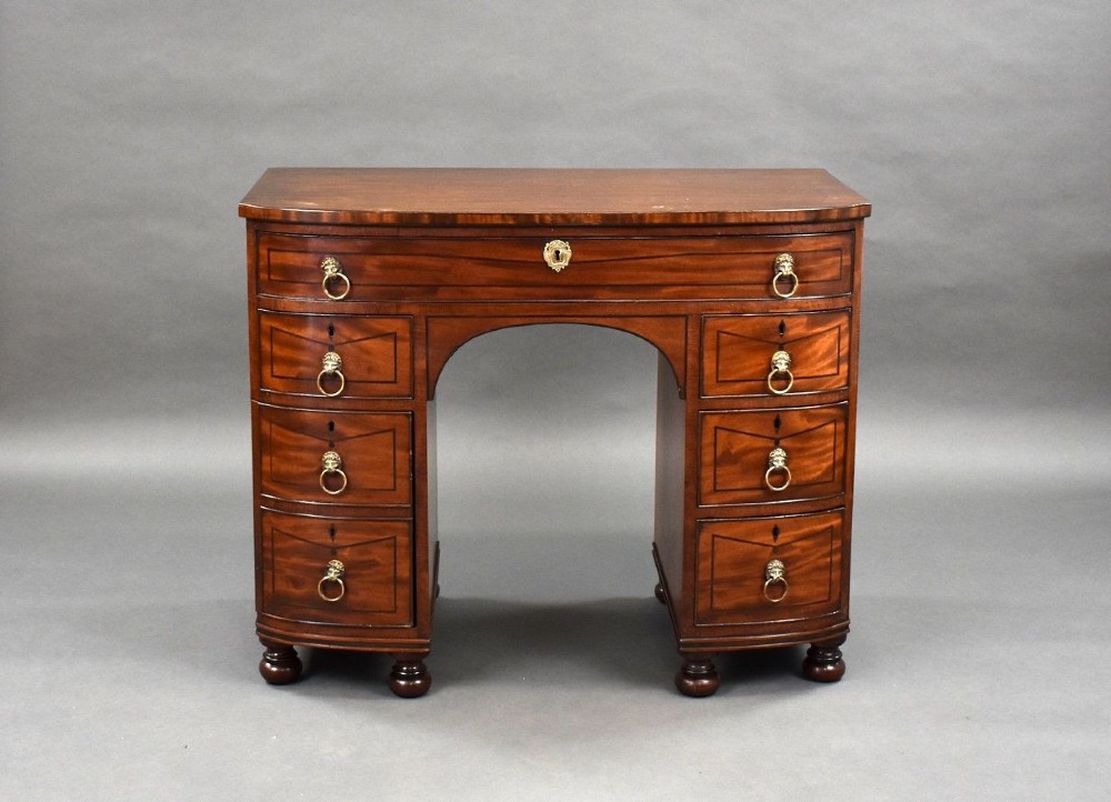 An antique Regency flame mahogany kneehole dressing chest with seven drawers, brass lion mask ring handles, and turned feet. View II