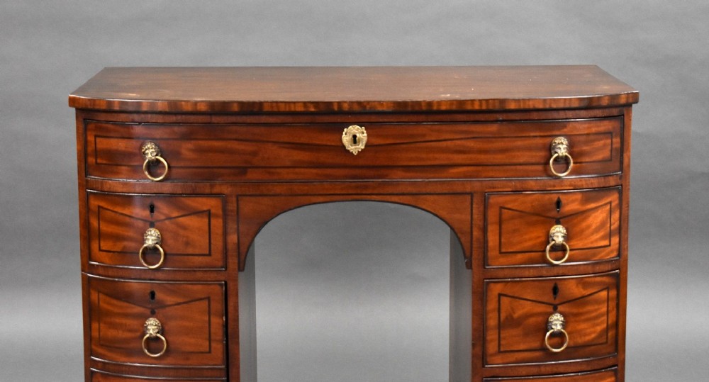 An antique Regency flame mahogany kneehole dressing chest with seven drawers, brass lion mask ring handles, and turned feet. View IV