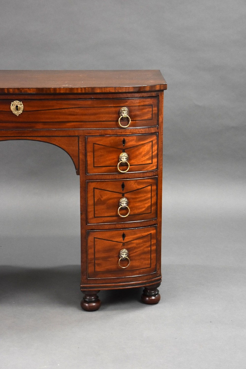 An antique Regency flame mahogany kneehole dressing chest with seven drawers, brass lion mask ring handles, and turned feet. View V