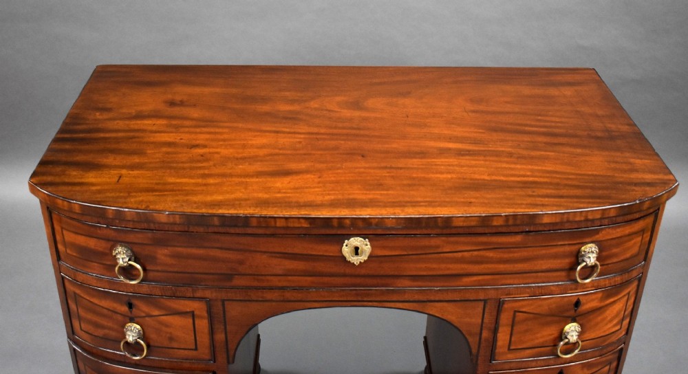 An antique Regency flame mahogany kneehole dressing chest with seven drawers, brass lion mask ring handles, and turned feet. View VI