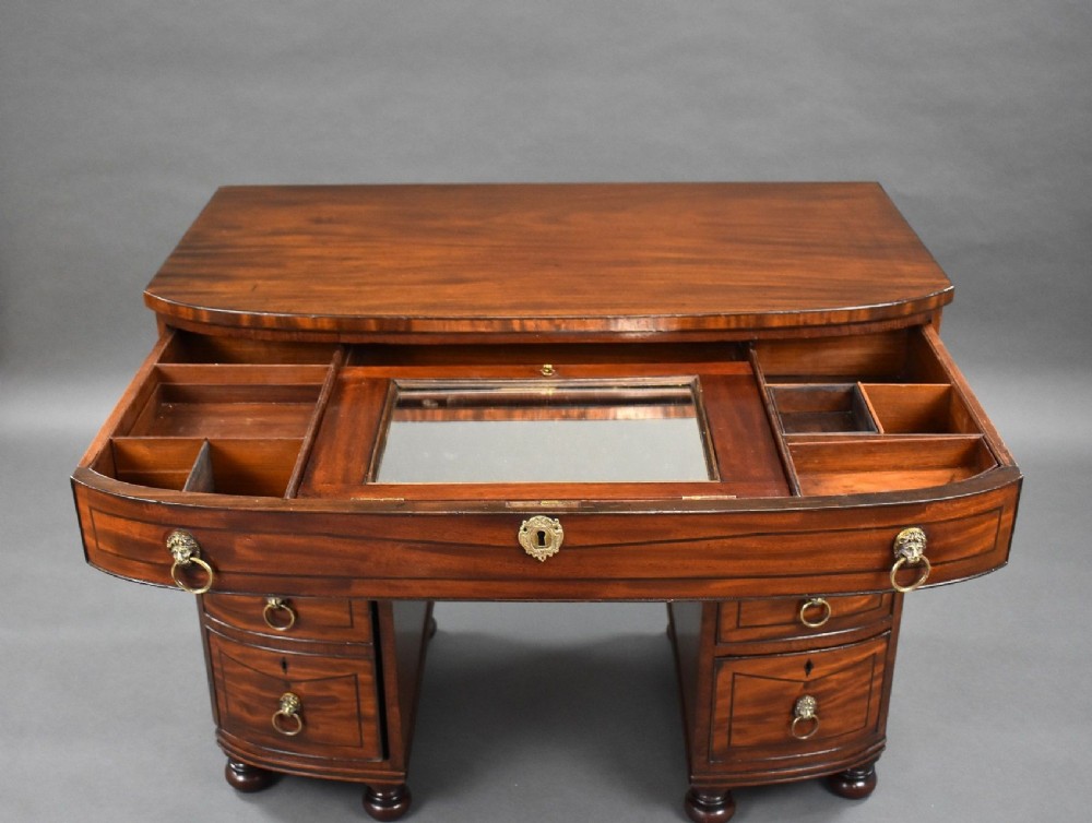 An antique Regency flame mahogany kneehole dressing chest with seven drawers, brass lion mask ring handles, and turned feet. View VII