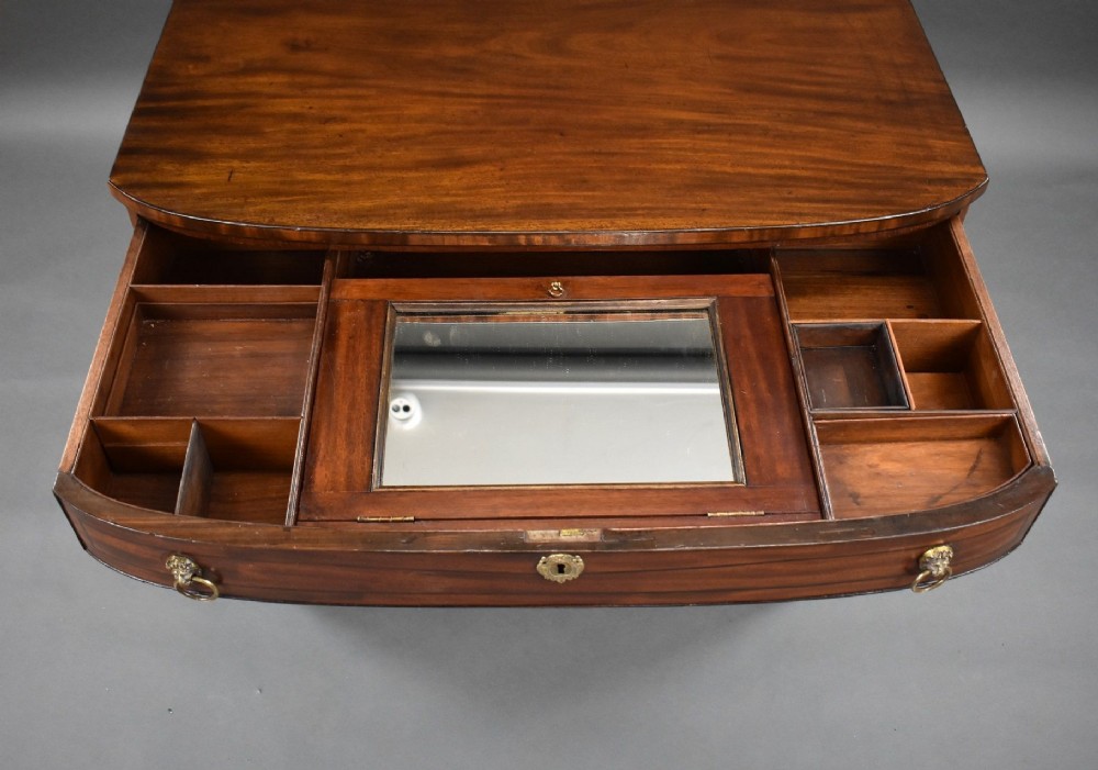 An antique Regency flame mahogany kneehole dressing chest with seven drawers, brass lion mask ring handles, and turned feet. View VIII