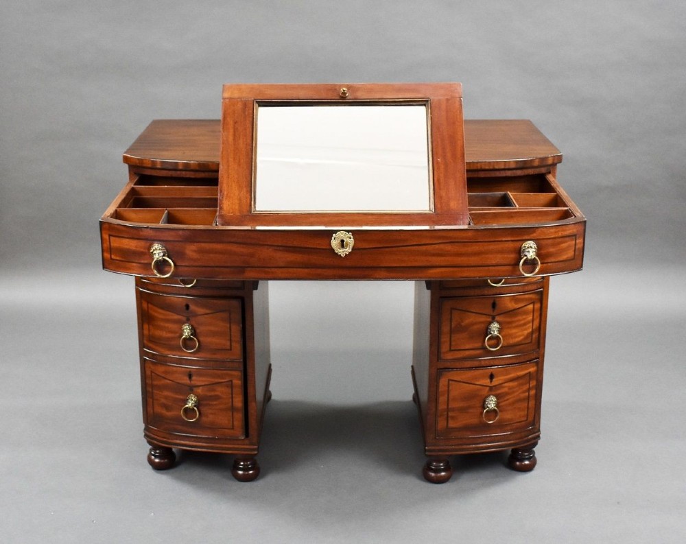 An antique Regency flame mahogany kneehole dressing chest with seven drawers, brass lion mask ring handles, and turned feet. View IX