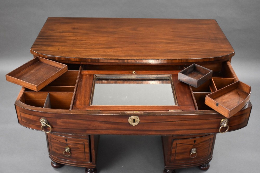 An antique Regency flame mahogany kneehole dressing chest with seven drawers, brass lion mask ring handles, and turned feet. View XI