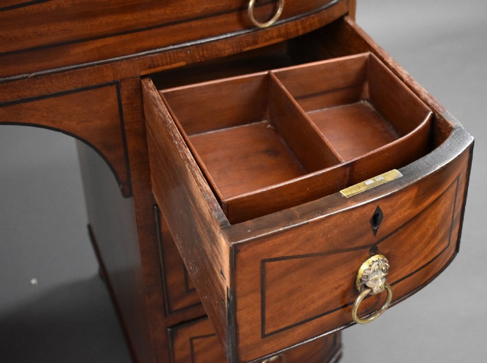 An antique Regency flame mahogany kneehole dressing chest with seven drawers, brass lion mask ring handles, and turned feet. View XII