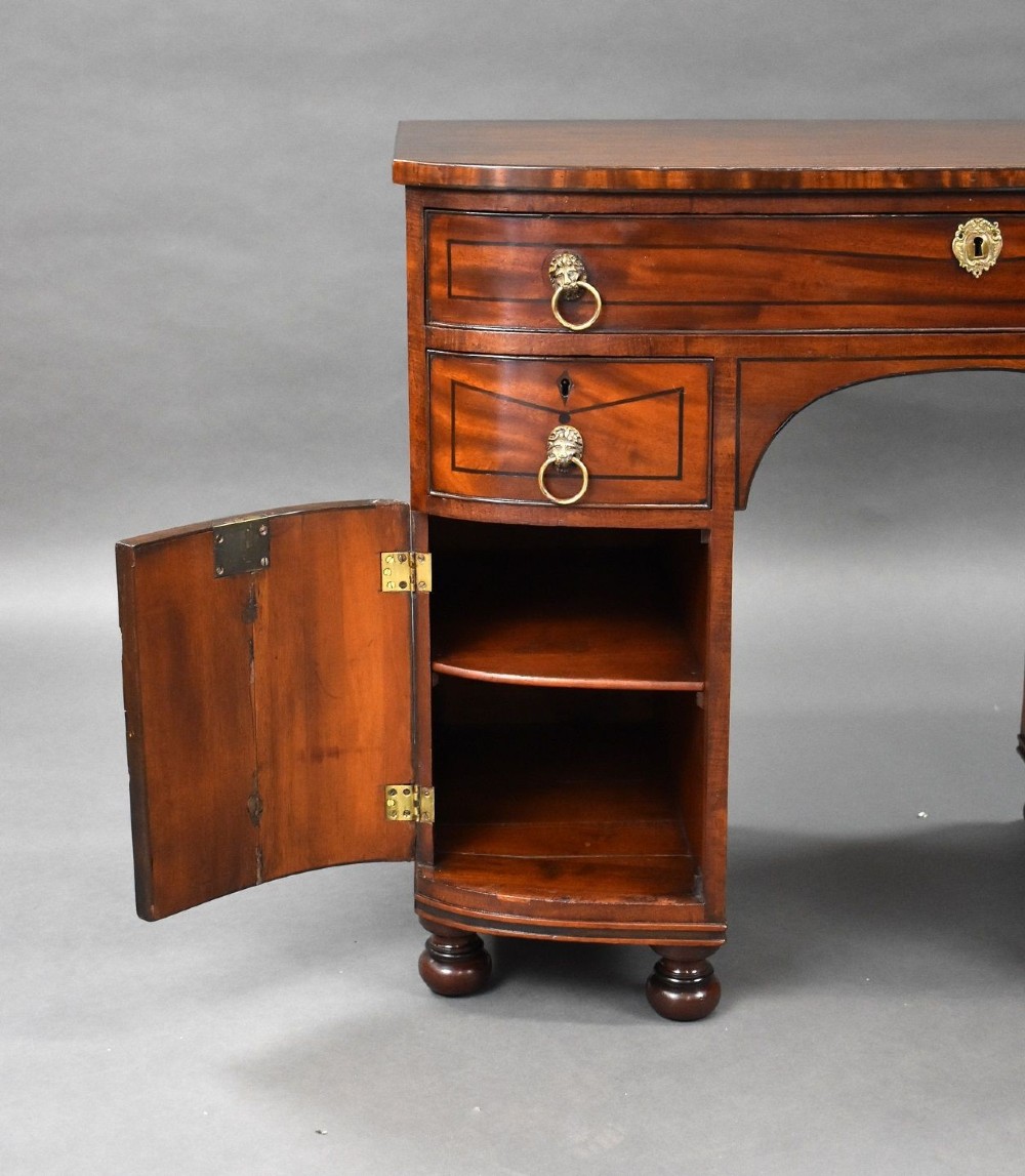 An antique Regency flame mahogany kneehole dressing chest with seven drawers, brass lion mask ring handles, and turned feet. View XIII