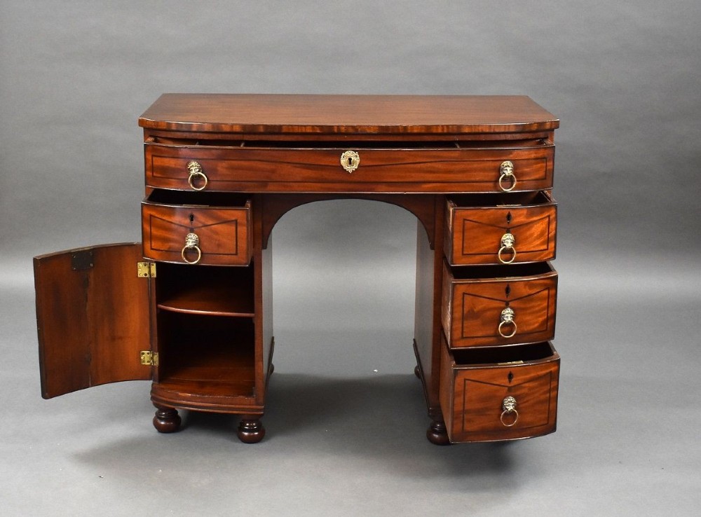 An antique Regency flame mahogany kneehole dressing chest with seven drawers, brass lion mask ring handles, and turned feet. View XIV