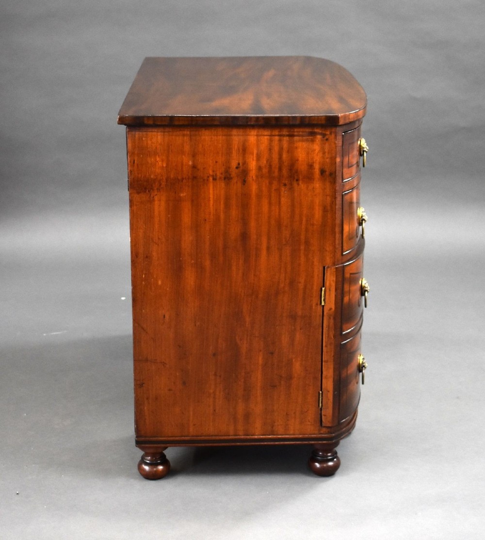 An antique Regency flame mahogany kneehole dressing chest with seven drawers, brass lion mask ring handles, and turned feet. View XV