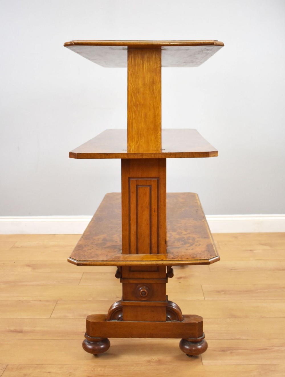A Victorian burr walnut three-tier telescopic dumbwaiter featuring adjustable shelves resting on carved trestle supports. View V