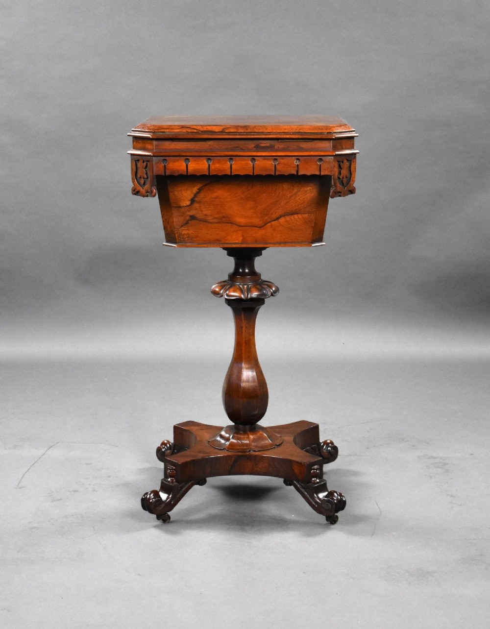 A William IV rosewood tea poy featuring a hinged lidded box top, carved openwork scrolls, a turned pedestal column, and a four-point base with scroll feet. View V