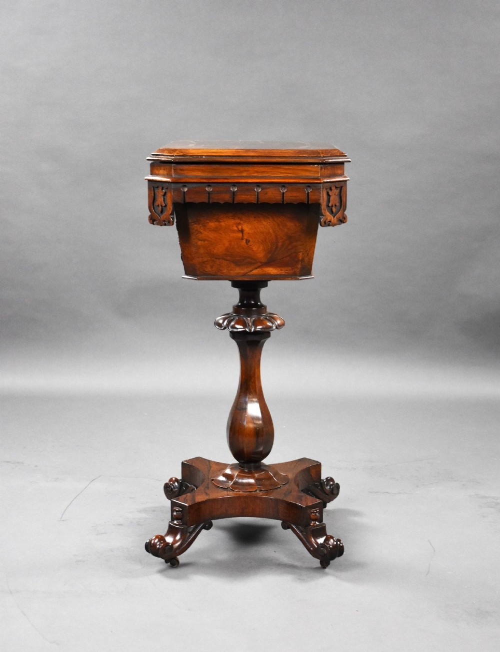 A William IV rosewood tea poy featuring a hinged lidded box top, carved openwork scrolls, a turned pedestal column, and a four-point base with scroll feet. View VI