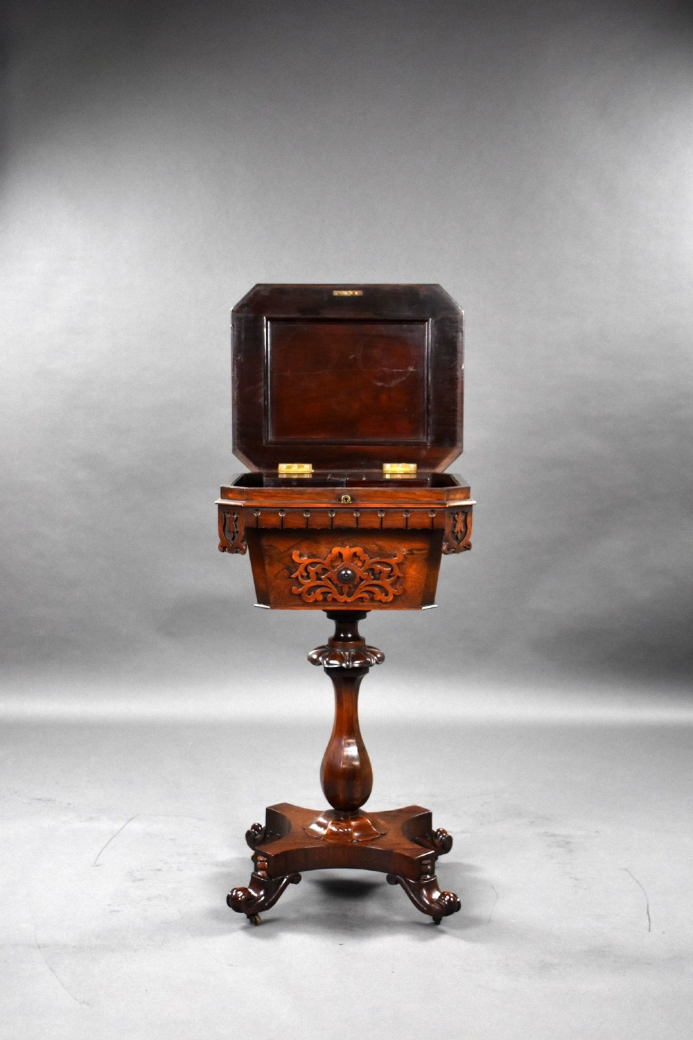 A William IV rosewood tea poy featuring a hinged lidded box top, carved openwork scrolls, a turned pedestal column, and a four-point base with scroll feet. View VII