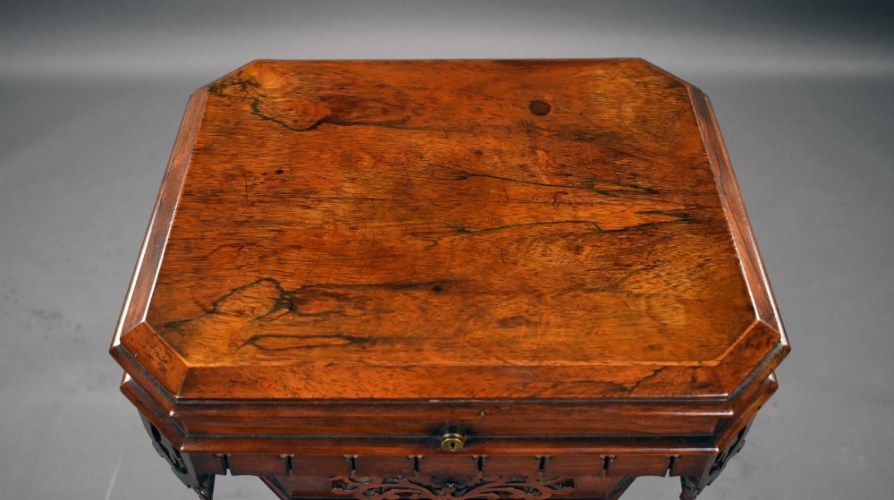 A William IV rosewood tea poy featuring a hinged lidded box top, carved openwork scrolls, a turned pedestal column, and a four-point base with scroll feet. View X